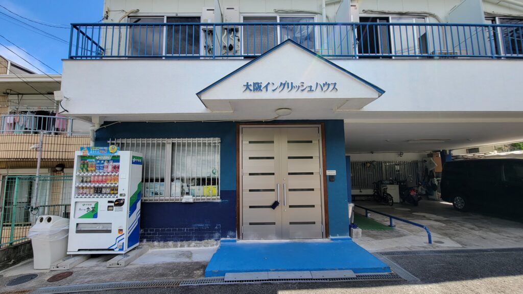 The front of Osaka English House with a double-door entrance and a clean, minimalist exterior, featuring blue accents